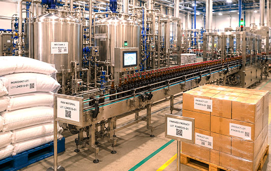 Food and beverage production line showing ingredient lots, processing equipment, bottled products, and finished goods with batch identification throughout the manufacturing process.
